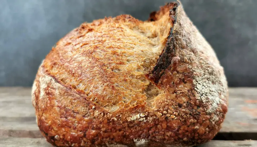 Ein rustikales Brot mit knuspriger Kruste liegt auf Holzbrettern. Schade, dass das Brot beim Backen nicht aufgegangen ist, aber es sieht trotzdem lecker aus.