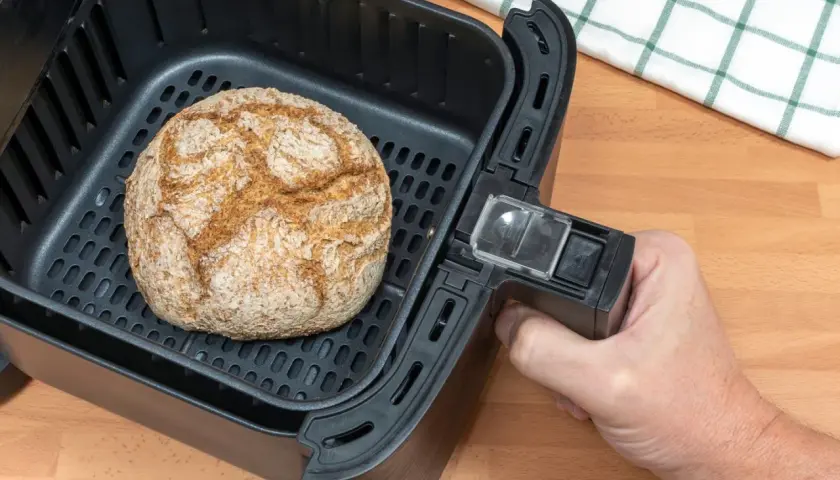 Ein goldbraunes Brot liegt im Korb eines Airfryers. Perfekt zum brot backen im airfryer für knusprigen Genuss.