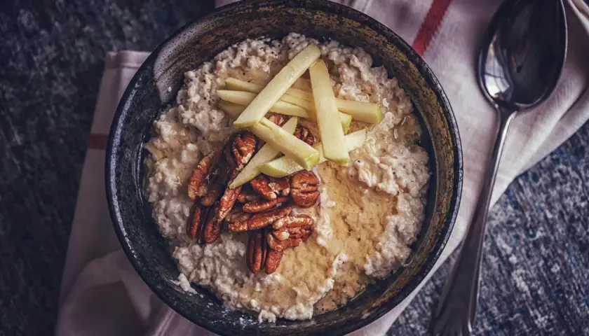 Schüssel mit cremigem Haferbrei, garniert mit Apfelspalten, Pekannüssen und Honig. Ein einfaches und leckeres Haferbrei Rezept für den Morgen.