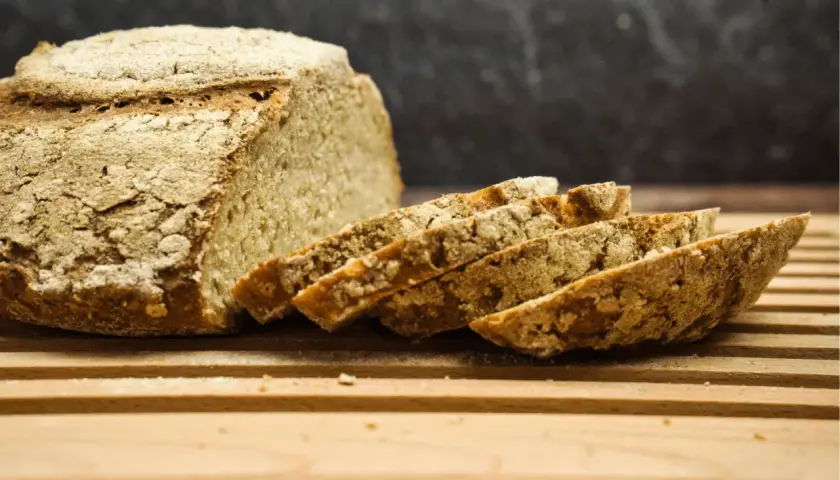 Frisch gebackenes Brot, angeschnitten auf einem Holzbrett. Die Kruste ist rustikal, die Scheiben zeigen die Porosität. Perfekt für die Frage: wie lange brotteig gehen lassen mit trockenhefe.
