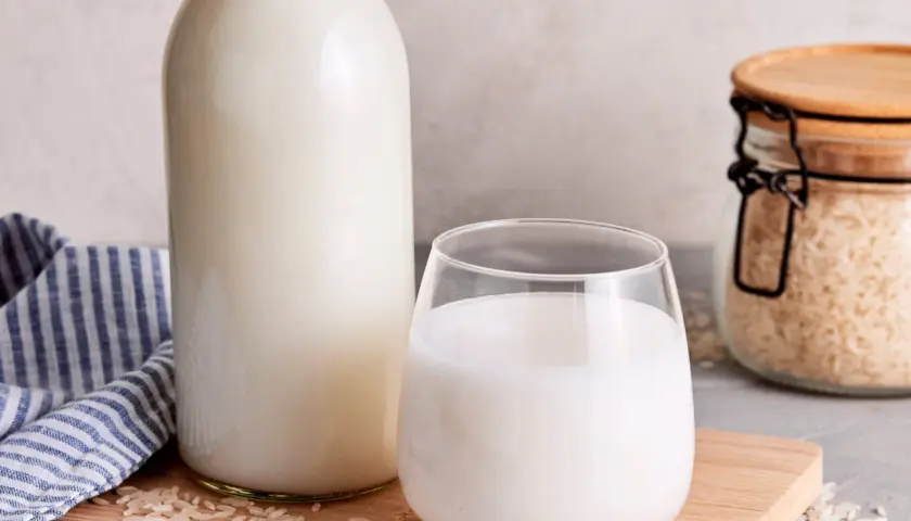 Frisch zubereitete Reismilch in einer Flasche und einem Glas, daneben Reis in einem Glasbehälter. So einfach ist es, Reismilch selber machen.