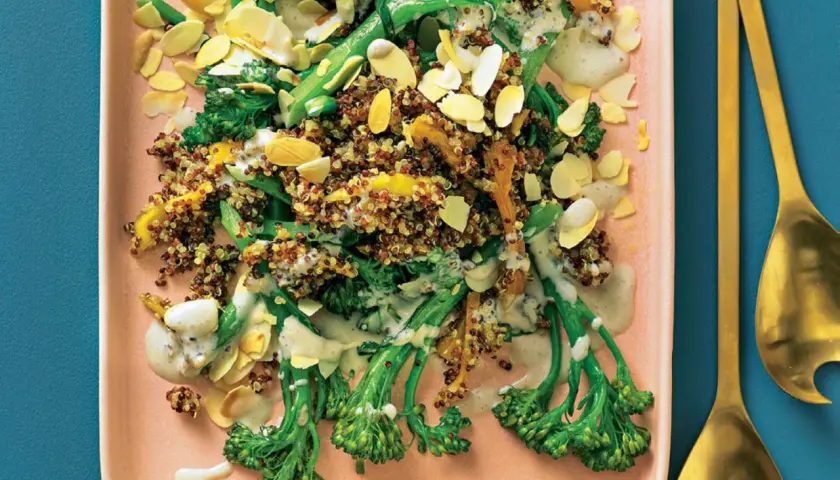 Bunter Quinoa-Salat mit wildem Brokkoli, Mandelsplittern und cremiger Sauce auf einem rosa Teller.