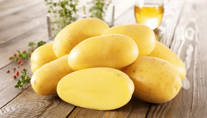 Ein Haufen frischer Kartoffeln, die an ihre Herkunft erinnern, liegen auf einem Holztisch. Daneben ein Glas Öl und Kräuter.