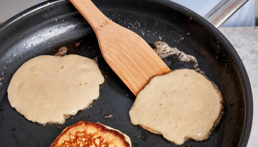 Buttermilch pancakes bräunen in der Pfanne, eine Holzspachtel wendet sie.