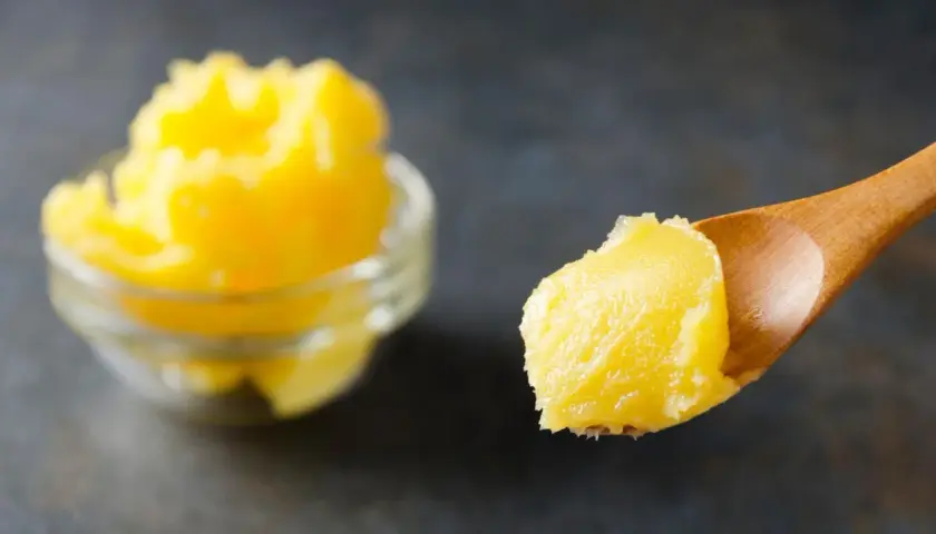 Goldgelbe, cremige vegane Butter auf einem Holzlöffel, daneben eine Schüssel voll. Perfekt, um vegane Butter selber machen zu können.