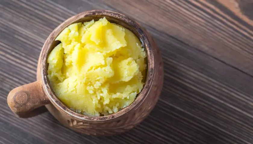 Ein Topf mit selbstgemachtem Ghee auf einem Holztisch. Das goldgelbe, cremige Ghee ist bereit zum Kochen.
