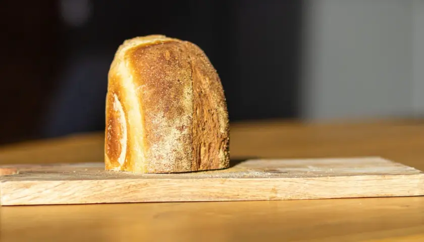 Ein frisch gebackenes Brot liegt auf einem Holzbrett. Die Kruste ist goldbraun und knusprig, was zeigt, wie wird brot saftig.