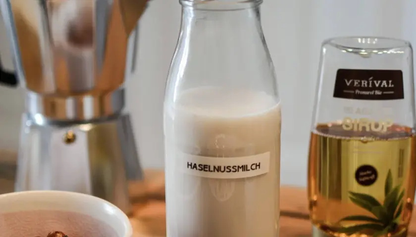 Zutaten für Haselnussmilch selber machen: Haselnüsse, Moka-Kanne, Agavendicksaft und eine Flasche mit selbstgemachter Haselnussmilch.