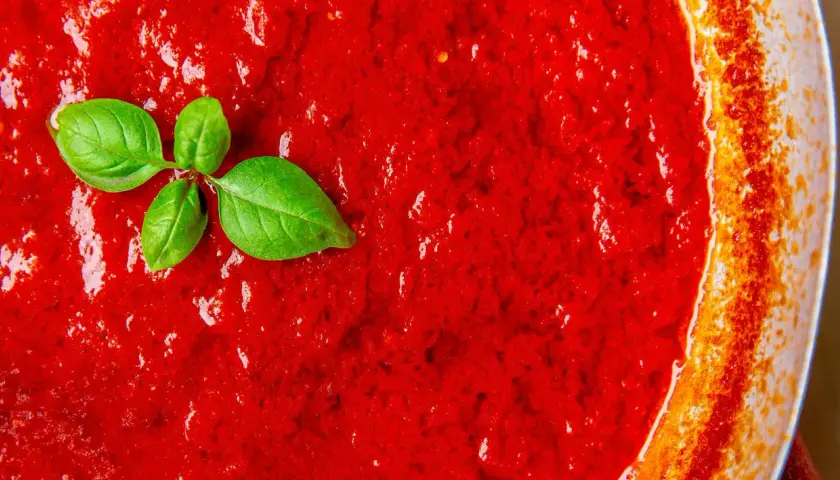 Frische Tomatensauce, die zeigt, wie einfach es ist, Tomatensauce selber zu machen. Ein Basilikumblatt liegt auf der leuchtend roten Masse.