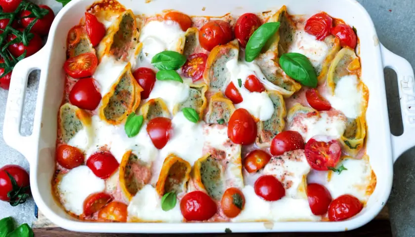Herzhafter Maultaschen Auflauf mit Kirschtomaten und geschmolzenem Mozzarella, garniert mit frischem Basilikum.