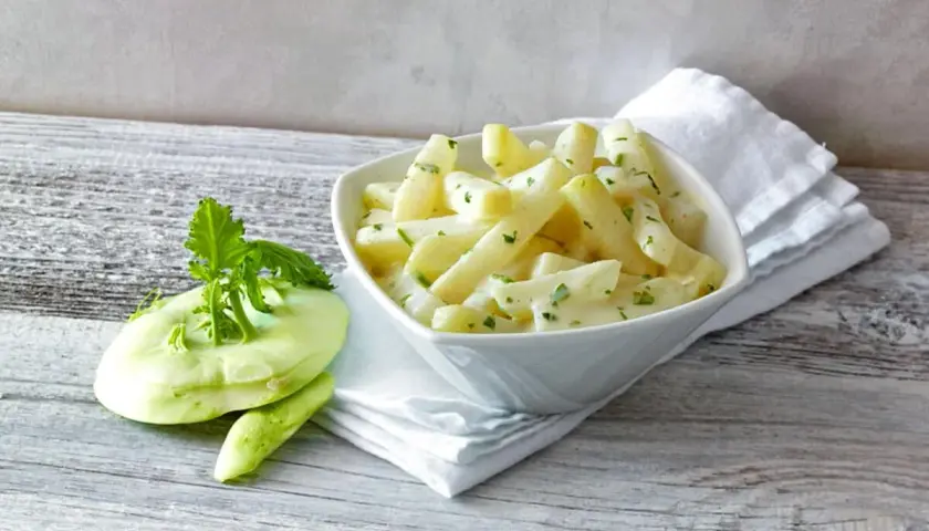 Kohlrabi kochen: Ein cremiges Gericht mit Kohlrabi-Stücken und frischer Petersilie, daneben ein roher Kohlrabi.