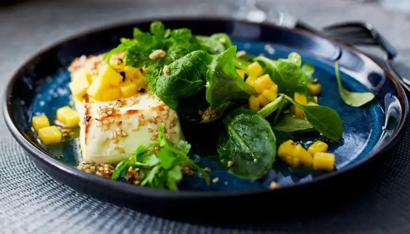 Vegane Vorspeisen: Gebratener Tofu mit Mango, Sesam und frischen Kräutern auf blauem Teller.