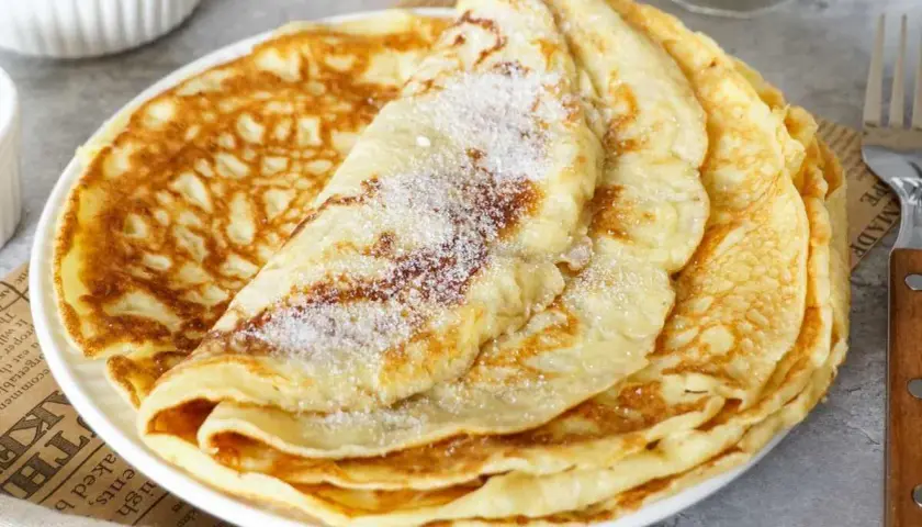 Ein Stapel goldbrauner Pfannkuchen, bestreut mit Zucker. Ein einfaches Pfannkuchen Rezept für jeden Tag.