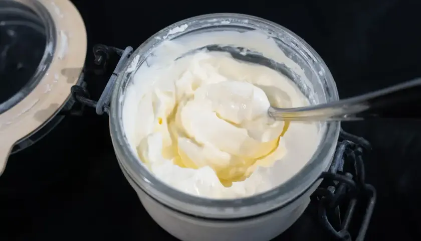 Creme fraiche selber machen ist einfach! Ein Löffel nimmt eine Portion der cremigen Masse aus dem Glas.
