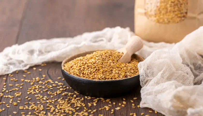 Schale mit goldenen Leinsamen und Holzschaufel, daneben ein Papiersack. Der Unterschied zwischen Leinsamen und Goldleinsamen wird hier visuell dargestellt.