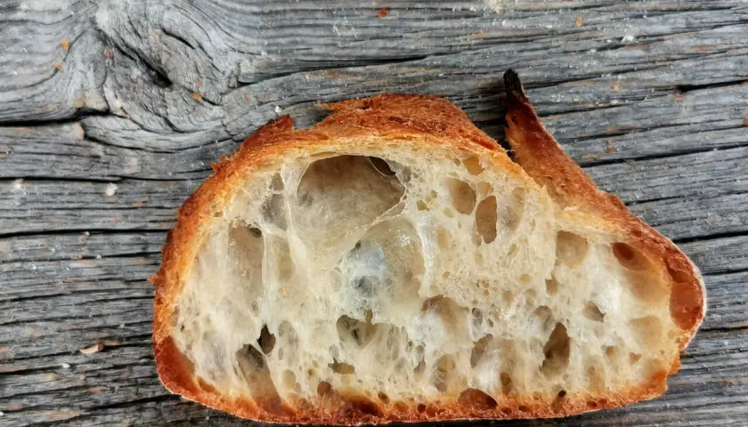 Ein Stück **selbstgebackenes Brot zu fest** mit großer Krume und knuspriger Kruste liegt auf einer alten Holzoberfläche.