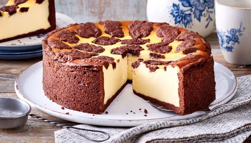 Ein saftiger russischer Zupfkuchen mit Schokoladenboden und cremiger Käsemasse, dekoriert mit dunklen Schokoladenstückchen.