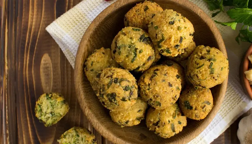 Schüssel mit frittierten Falafel-Bällchen, die aus frischen falafel zutaten zubereitet wurden. Daneben liegen Knoblauch und Kräuter.