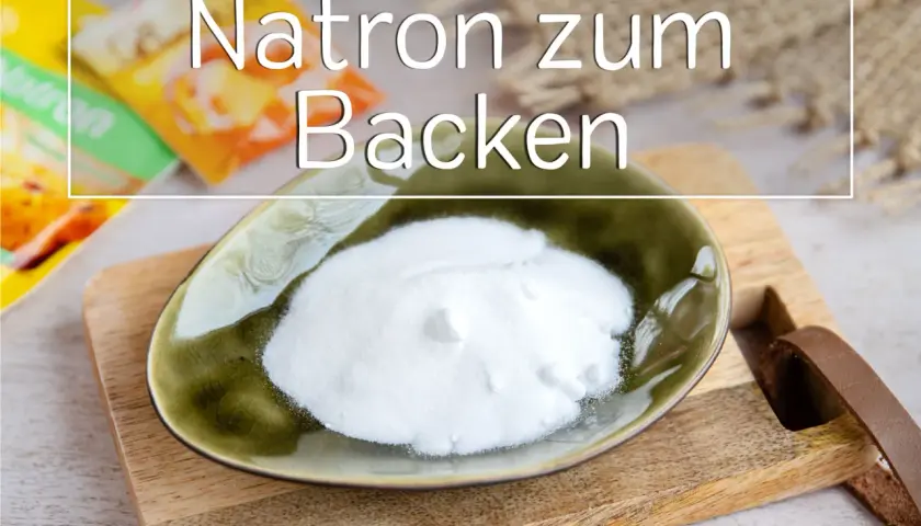 Eine Schale mit weißem Natron zum Backen steht auf einem Holzbrett. Im Hintergrund sind Packungen zu sehen.