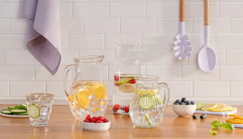 Erfrischendes infused wasser mit Zitrone, Gurke und Beeren in Glaskaraffen und einem Glas.