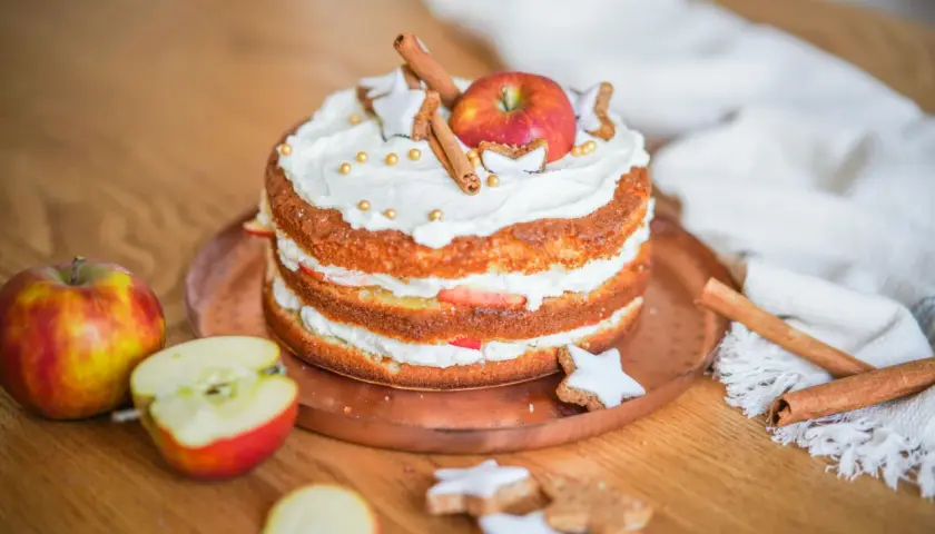 Ein Apfelkuchen, der mit Sahne, Zimtstangen, Sternen-Plätzchen und goldenen Perlen verziert ist. So lässt sich eine Backmischung aufpeppen!