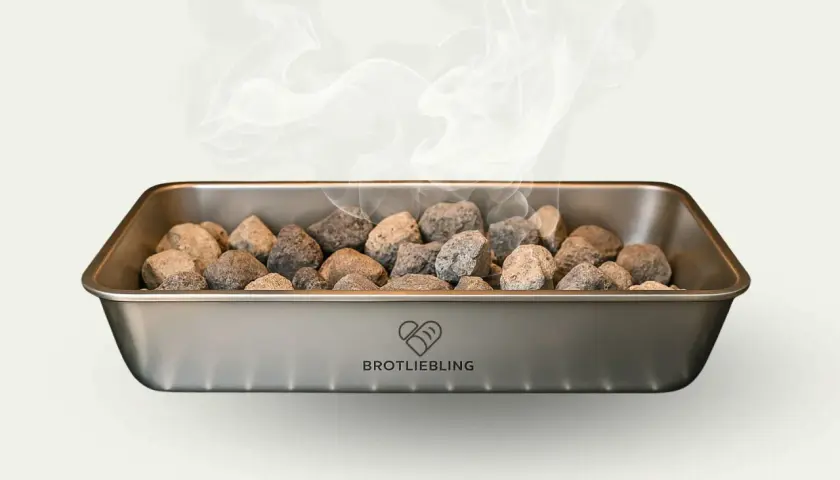 Dampf steigt aus einem Metallbehälter mit Steinen auf. Für knuspriges Brot muss man Wasser in den Ofen geben.