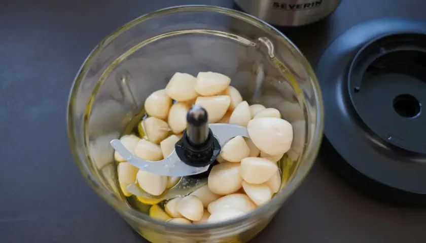 Ein Glas-Zerkleinerer mit vielen geschälten Knoblauchzehen und etwas Öl. Perfekt für ein schnelles Knoblauchpaste Rezept.