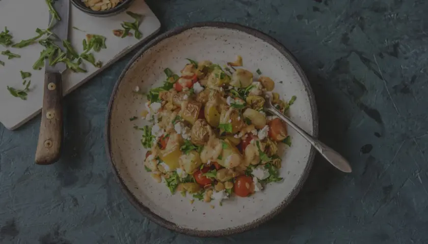 Herzhafter Salat mit bratkartoffeln aus rohen kartoffeln, Feta, Kirschtomaten und Rucola, garniert mit Mandelsplittern.
