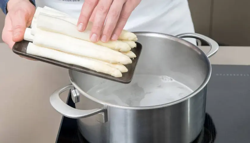 Frische weiße Spargelstangen werden in kochendes Wasser gegeben. Ob mit oder ohne Deckel, das Spargel kochen beginnt jetzt.