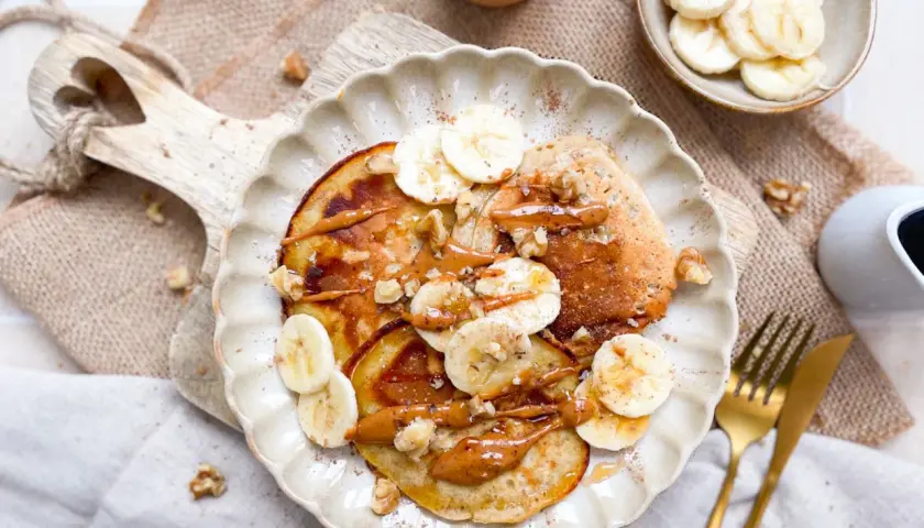 Bananen Pancakes ohne Ei, garniert mit Bananenscheiben, Walnüssen und einer cremigen Sauce. Ein köstlicher Start in den Tag.