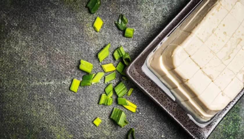 Seidentofu selber machen: Ein Block Seidentofu in einer Schale, daneben geschnittene Frühlingszwiebeln auf dunklem Untergrund.