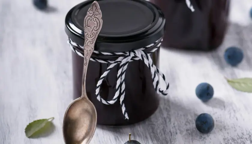 Glas mit Schlehenmarmelade, Löffel und Schlehen. Perfekt für Schlehen Rezepte.
