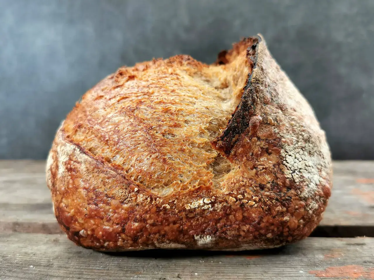 Ein rustikales Brot mit knuspriger Kruste liegt auf Holzbrettern. Schade, dass das Brot beim Backen nicht aufgegangen ist, aber es sieht trotzdem lecker aus.