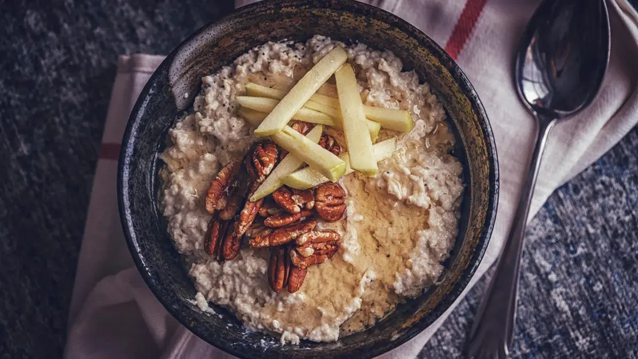 Schüssel mit cremigem Haferbrei, garniert mit Apfelspalten, Pekannüssen und Honig. Ein einfaches und leckeres Haferbrei Rezept für den Morgen.