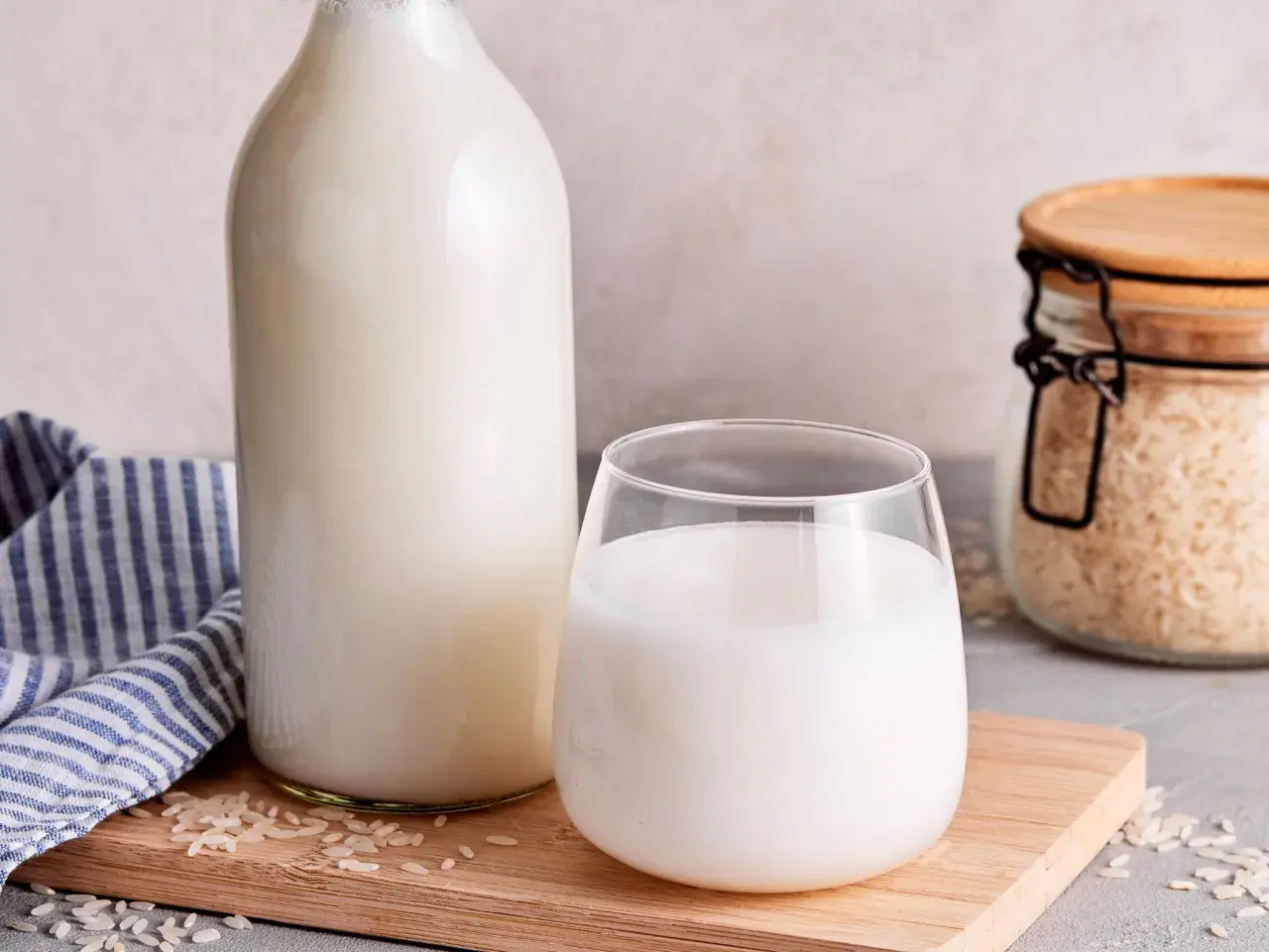 Frisch zubereitete Reismilch in einer Flasche und einem Glas, daneben Reis in einem Glasbehälter. So einfach ist es, Reismilch selber machen.
