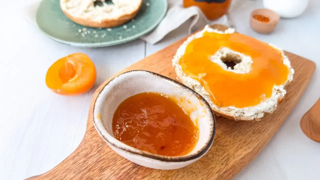 Ein Bagel mit Frischkäse und leckerer Aprikosenmarmelade, die Lust auf das Aprikosenmarmelade Rezept macht. Daneben eine halbe Aprikose.