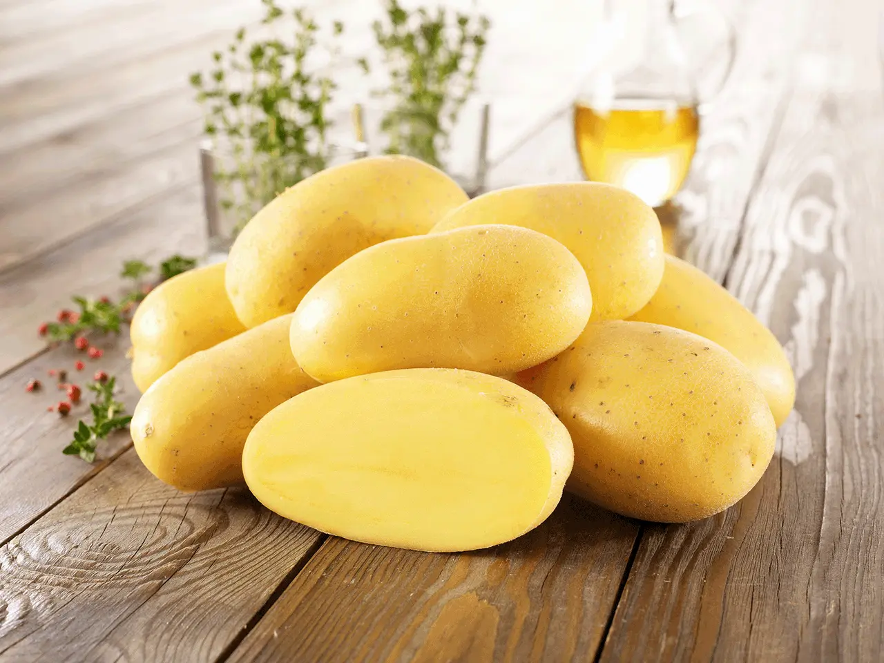 Ein Haufen frischer Kartoffeln, die an ihre Herkunft erinnern, liegen auf einem Holztisch. Daneben ein Glas Öl und Kräuter.