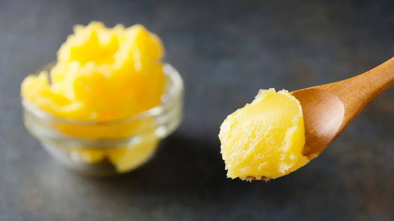 Goldgelbe, cremige vegane Butter auf einem Holzlöffel, daneben eine Schüssel voll. Perfekt, um vegane Butter selber machen zu können.