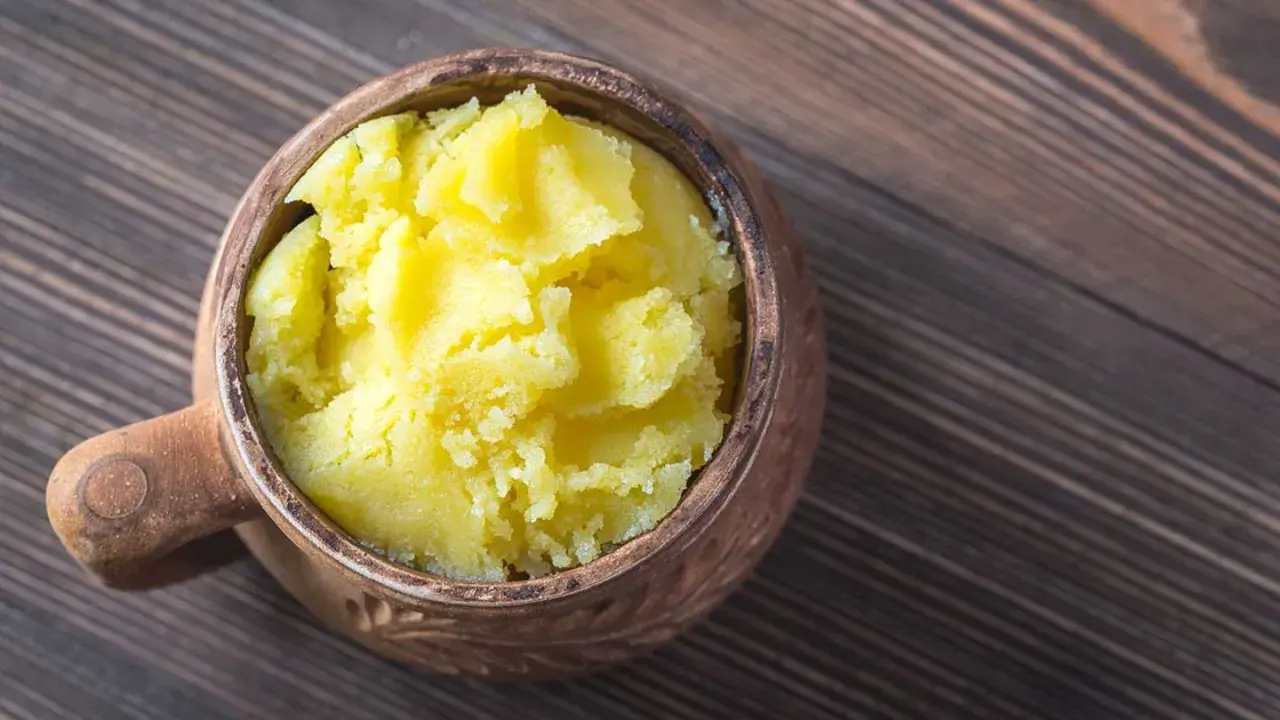 Ein Topf mit selbstgemachtem Ghee auf einem Holztisch. Das goldgelbe, cremige Ghee ist bereit zum Kochen.
