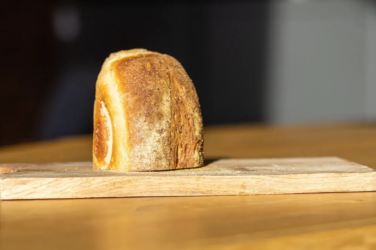 Ein frisch gebackenes Brot liegt auf einem Holzbrett. Die Kruste ist goldbraun und knusprig, was zeigt, wie wird brot saftig.