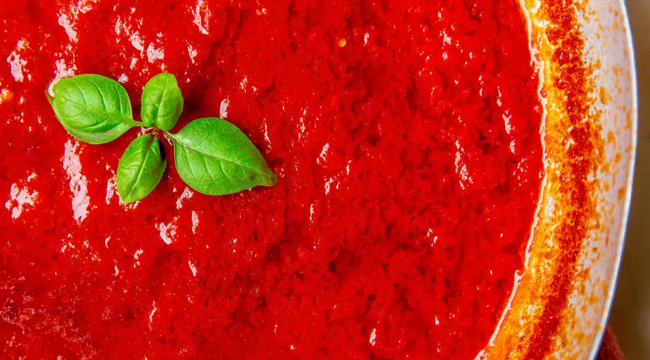 Frische Tomatensauce, die zeigt, wie einfach es ist, Tomatensauce selber zu machen. Ein Basilikumblatt liegt auf der leuchtend roten Masse.