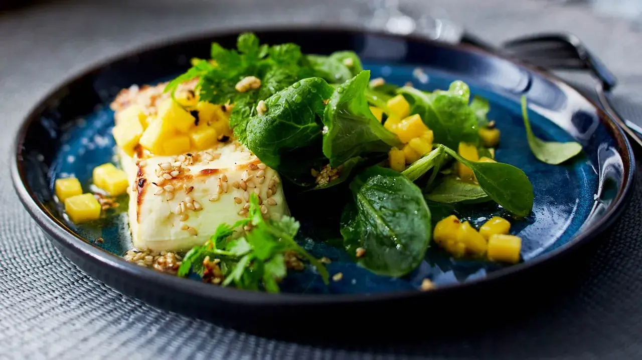 Vegane Vorspeisen: Gebratener Tofu mit Mango, Sesam und frischen Kräutern auf blauem Teller.