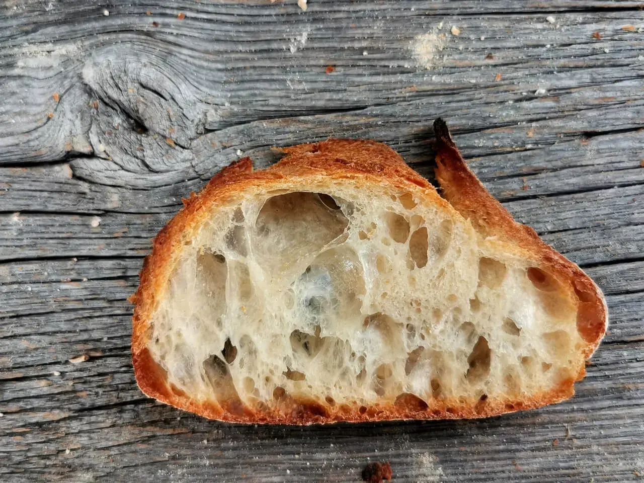Ein Stück **selbstgebackenes Brot zu fest** mit großer Krume und knuspriger Kruste liegt auf einer alten Holzoberfläche.