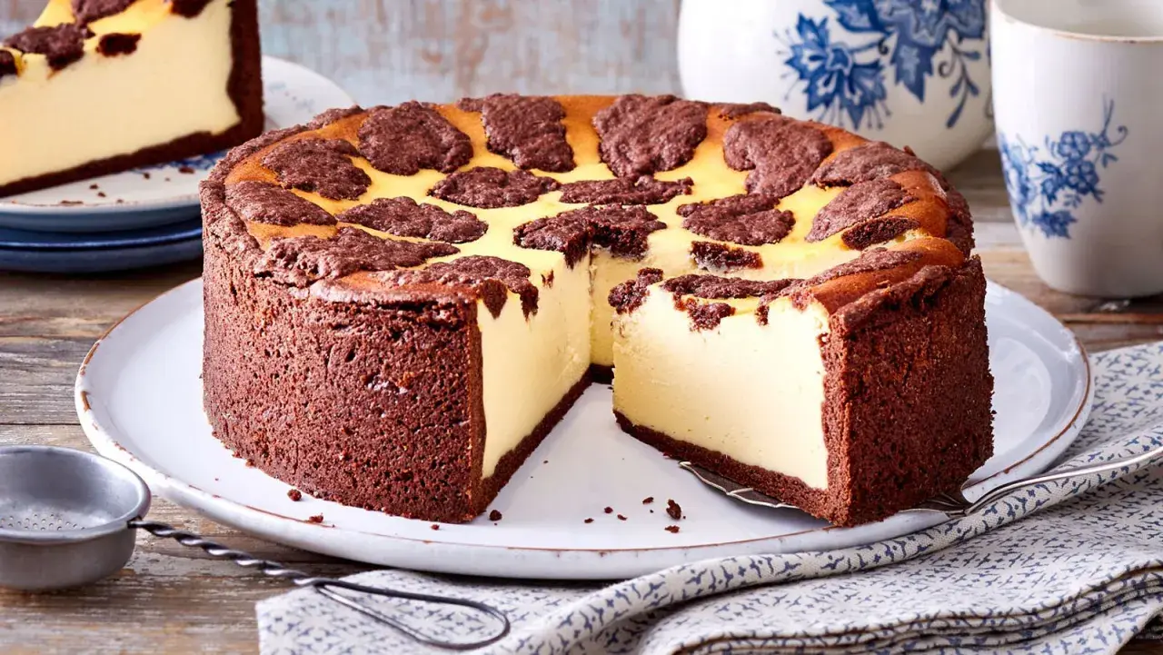 Ein saftiger russischer Zupfkuchen mit Schokoladenboden und cremiger Käsemasse, dekoriert mit dunklen Schokoladenstückchen.
