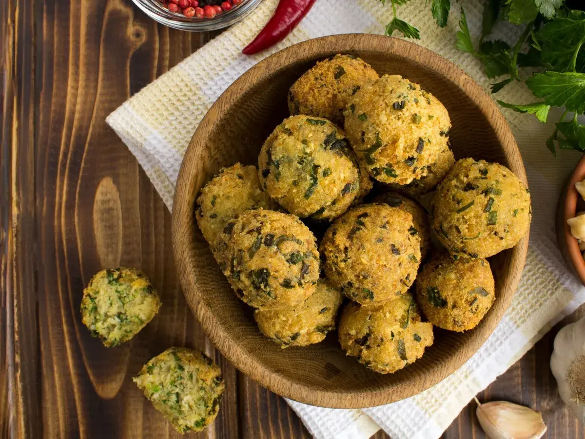 Schüssel mit frittierten Falafel-Bällchen, die aus frischen falafel zutaten zubereitet wurden. Daneben liegen Knoblauch und Kräuter.