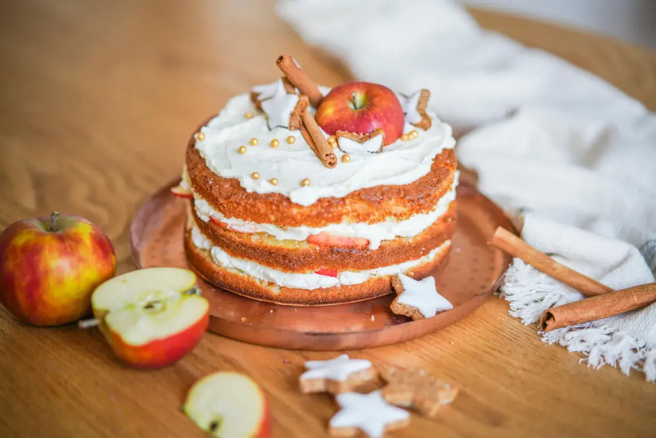 Ein Apfelkuchen, der mit Sahne, Zimtstangen, Sternen-Plätzchen und goldenen Perlen verziert ist. So lässt sich eine Backmischung aufpeppen!