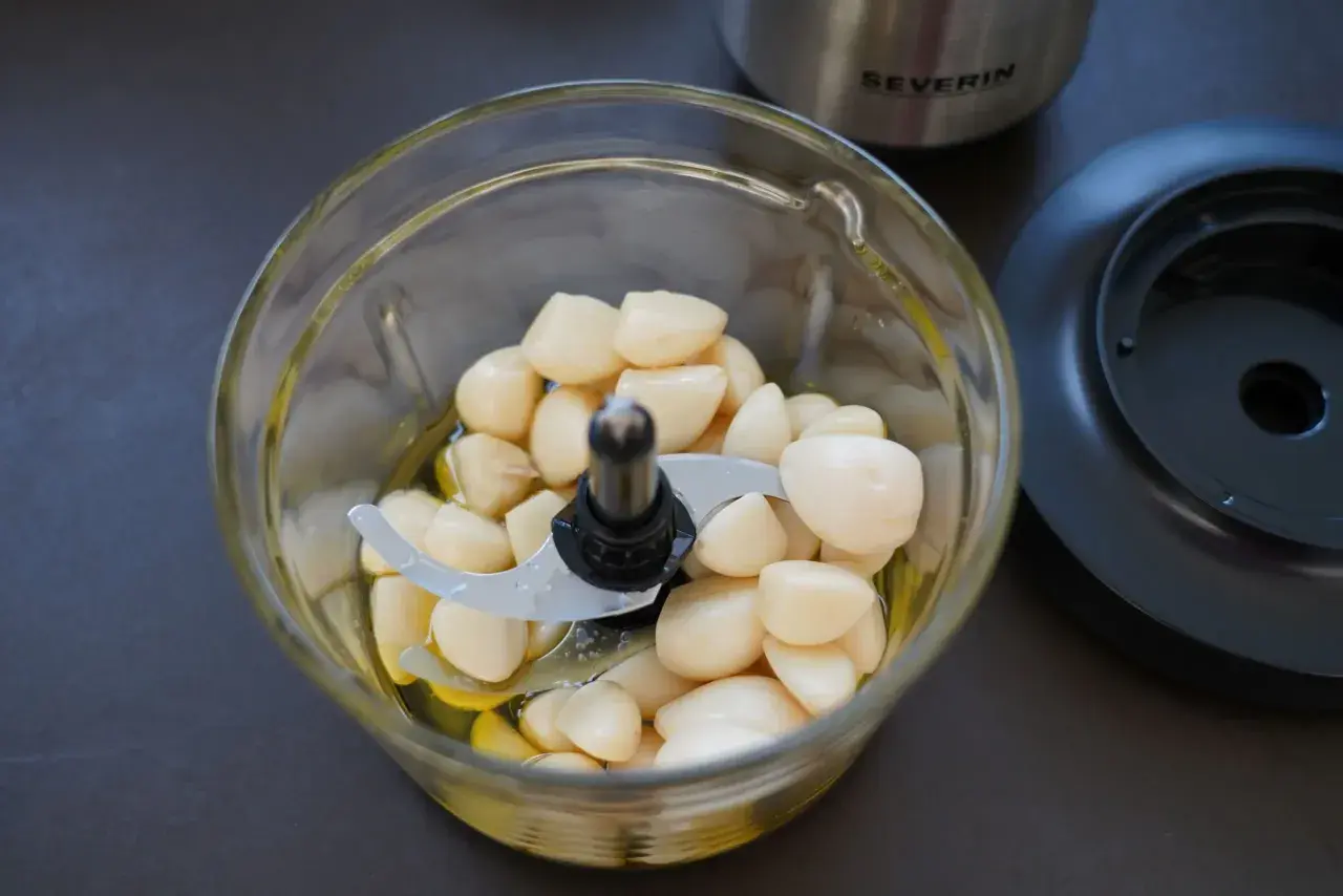 Ein Glas-Zerkleinerer mit vielen geschälten Knoblauchzehen und etwas Öl. Perfekt für ein schnelles Knoblauchpaste Rezept.