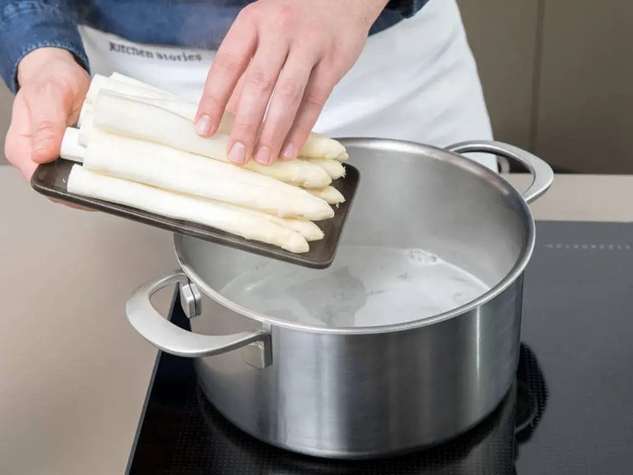 Frische weiße Spargelstangen werden in kochendes Wasser gegeben. Ob mit oder ohne Deckel, das Spargel kochen beginnt jetzt.