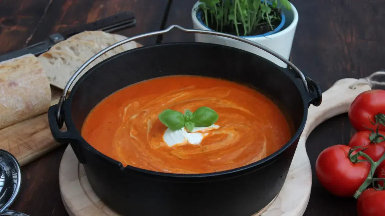 Ein köstliches Tomatensuppe Rezept mit frischen Tomaten, garniert mit Basilikum und einem Klecks Sahne, serviert in einem Gusseisentopf mit Brot.
