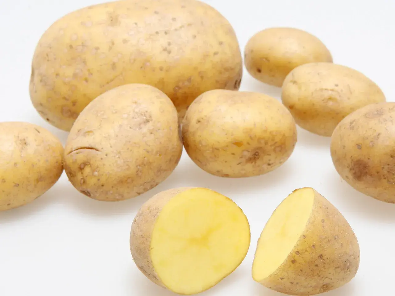 Mehrere Kartoffeln, eine davon halbiert, zeigen ihren gelben Fruchtfleisch. Der hohe Kartoffel Wassergehalt macht sie saftig.